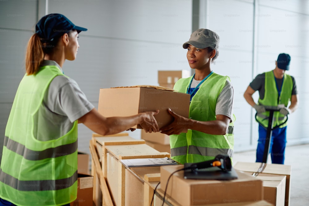 African American warehouse foreman giving to female worker packages for shipment from storage room.